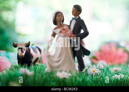 Bride and Groom figurines standing dans le champ de fleurs en plastique, à proximité de vache Banque D'Images