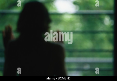 Femme debout à la fenêtre de sortie, vue arrière, defocused Banque D'Images