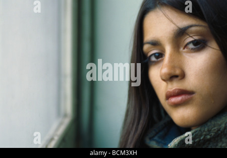 Jeune femme près de fenêtre, looking at camera, fronçant Banque D'Images