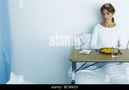 Woman reclining in hospital bed, plateau à repas sur ses genoux, regardant vers le bas Banque D'Images