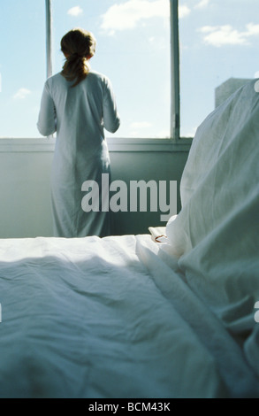 Woman standing in hospital room, looking out window, vue arrière Banque D'Images