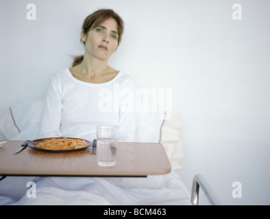 Femme assise jusqu'au lit d'hôpital, à l'écart de plateau à repas Banque D'Images