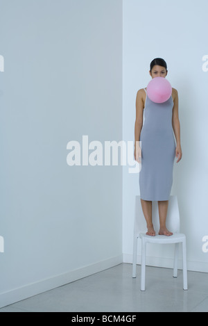 Femme debout sur une chaise, holding balloon en bouche, looking at camera Banque D'Images