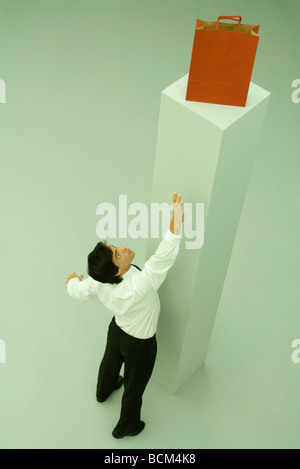 Homme debout à côté de piédestal, atteignant pour sac de shopping, high angle view Banque D'Images