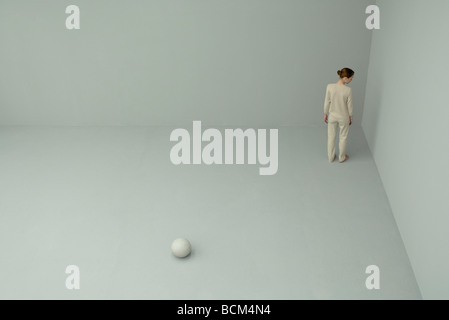 Femme debout en coin avec dos tourné à la caméra, une grande boule blanche sur le sol derrière elle Banque D'Images