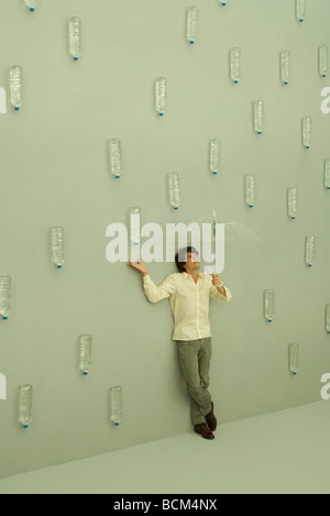 Man holding umbrella, bouteilles d'eau tombent comme des gouttes de pluie autour de lui Banque D'Images