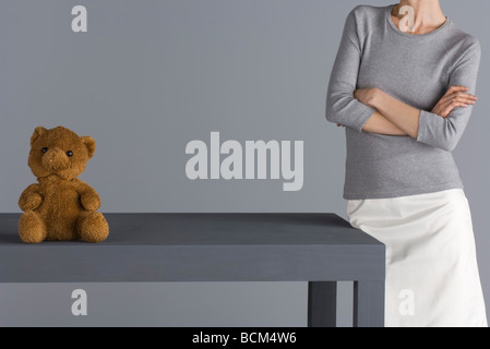 Femme debout à côté de table avec ours assis sur elle, les bras croisés, cropped view Banque D'Images