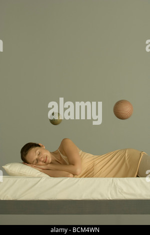 Woman sleeping in bed, deux sphères flottant dans l'air au-dessus de sa Banque D'Images