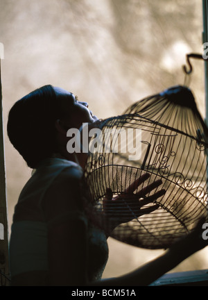 Woman leaning out window, holding empty birdcage, looking up Banque D'Images