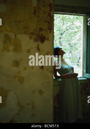 Woman leaning out fenêtre avec les mains sur l'estomac, jusqu'à Banque D'Images