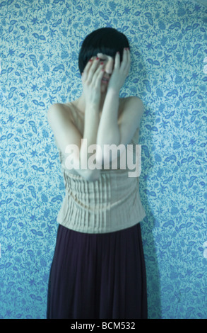 Woman leaning against wall, couvrant le visage avec les mains Banque D'Images