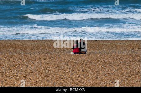 Un homme et une femme assis ensemble sur la plage de galets à Brighton, dans le Sussex. Photo par Gordon 1928 Banque D'Images
