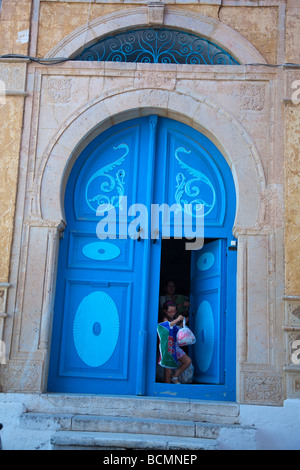 Une fille sort de la porte de sa maison à Sidi Bou Saïd, une charmante ville du nord de la Tunisie de couleur blanche et bleu. Banque D'Images