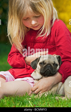 Petite fille avec le pug dog puppy - sitting on meadow Banque D'Images