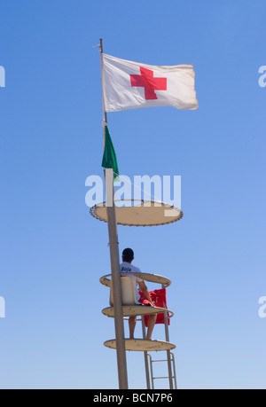 Lifeguard en devoir, qui est situé dans la tour avec drapeau de la Croix-Rouge et parasol à Rosas Costa Brava Catalogne Espagne Espana Banque D'Images