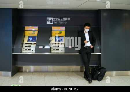 Un masque de gaze de banlieue avec l'aide d'un téléphone portable à côté de la machine à ticket de métro station de métro à Tokyo Japon Banque D'Images
