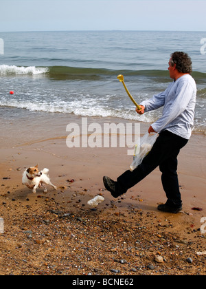 Un homme sur la plage lançant une boule d'exercer un chien sur une jambe Banque D'Images