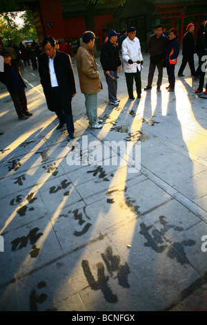 Les badauds observer le travail de personnes qui pratiquent la calligraphie à l'aide du pinceau et l'eau, le parc Beihai, Beijing, Chine Banque D'Images