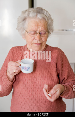 Frau dans votre Siebzigern steht in der Küche und ihre schluckt Tabletten Banque D'Images