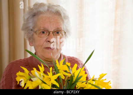 Frau dans votre Siebzigern steht im Wohnzimmer und hält einen Strauß Osterglocken Narcissus pseudonarcissus Banque D'Images