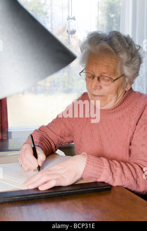 Frau dans votre Siebzigern sitzt am Schreibtisch und einen schreibt brève Banque D'Images