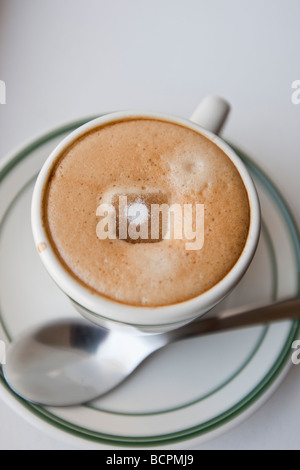 Vue de dessus d'un cube de sucre fondre dans la mousse d'un café expresso chaud boire dans une tasse avec une cuillère en métal Banque D'Images