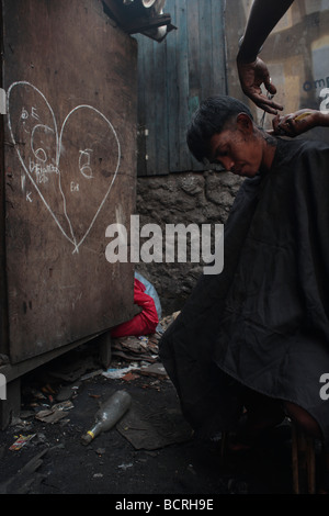 Un garçon obtient sa coupe dans les bidonvilles de Tamabakan, Tondo, Philippines Banque D'Images