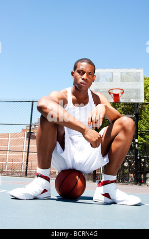 African American male sportif beau joueur de basket-ball avec l'attitude de blanc vêtue assise sur son ballon piscine en été Banque D'Images