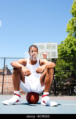 African American male sportif beau joueur de basket-ball avec l'attitude de blanc vêtue assise sur son ballon piscine en été Banque D'Images