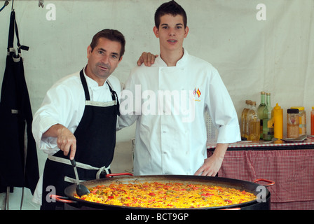 L'homme et l'assistant en remuant grande poêle de paella au marché continental Banque D'Images