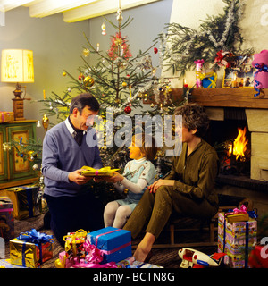 Monsieur COUPLE DONNANT DES CADEAUX DE NOËL À PETITE FILLE SOUS L'ARBRE Banque D'Images