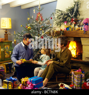 Monsieur COUPLE DONNANT DES CADEAUX DE NOËL À PETITE FILLE SOUS L'ARBRE Banque D'Images