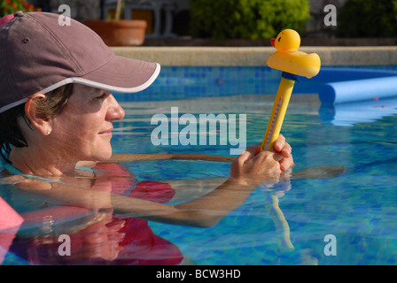 Woman in swimming pool à la recherche à la température de l'eau sur un thermomètre en forme de canard, Espagne Banque D'Images