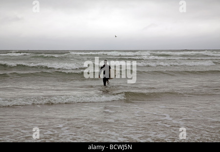 Accompagné seulement par un pélican brun un surfeur solitaire pénètre dans l'eau près de Rockaway Beach, sur la côte du Pacifique de l'Oregon Banque D'Images