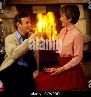 COUPLE DE trinquer avec les verres de champagne et de l'échange CADEAU DE NOËL PAR CHEMINÉE Banque D'Images