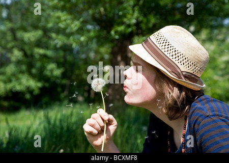 Teenage boy soufflant sur un pissenlit Banque D'Images