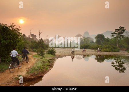 Les enfants à vélo à l'école à l'aube ; l'heure de pointe dans la campagne près de Vang Vieng, Laos Banque D'Images