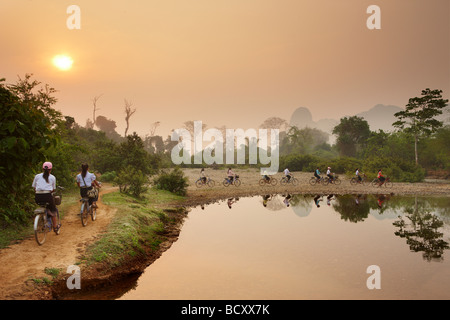 Les cyclistes à l'aube, l'heure de pointe dans la campagne près de Vang Vieng, Laos Banque D'Images