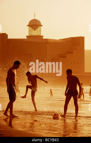 Trois hommes jouent au football sur la plage de Las Canteras en face de l'Auditorium Alfredo Krauis Banque D'Images