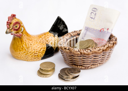 Des crédits sont mis à côté d'une poule en céramique. Une poule similaire a été utilisée pour la famille pour placer de l'argent dans la télévision britannique,pain série Banque D'Images