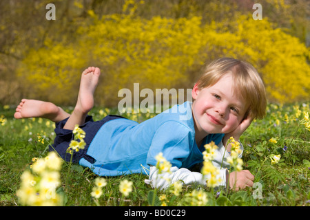 Garçon couché dans l'herbe avec des fleurs de printemps Banque D'Images