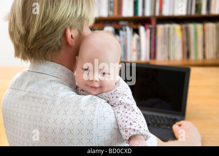 Père working on laptop carrying baby Banque D'Images