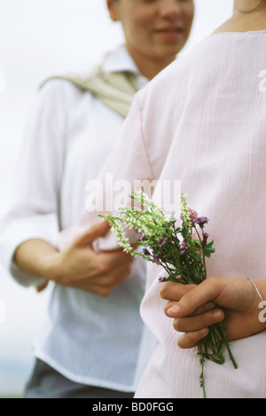 Girl holding bouquet de fleurs sauvages derrière le dos, embrassant mère Banque D'Images