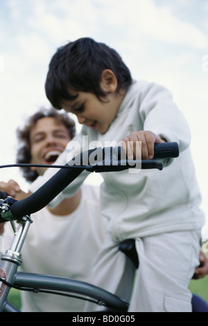 Petit garçon à vélo trop grand pour lui, père de rire en arrière-plan Banque D'Images