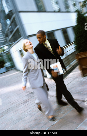 Businessman and businesswoman walking together in conversation, woman laughing Banque D'Images