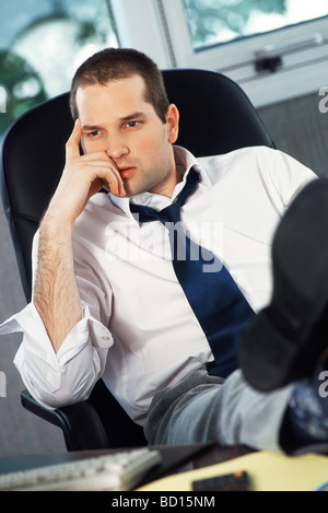 L'homme avec les pieds sur un bureau holding head looking away Banque D'Images