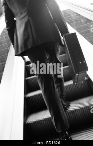 Businessman carrying briefcase escalator ascendant, vue arrière Banque D'Images