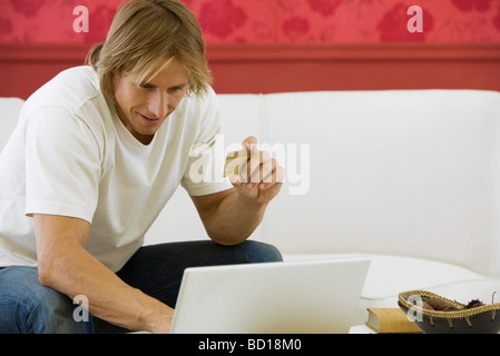Homme assis sur le canapé, faisant de l'achat en ligne par carte de crédit Banque D'Images