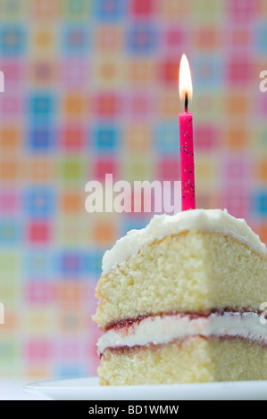 Tranche de gâteau d'anniversaire avec une bougie allumée contre un fond pastel coloré Banque D'Images