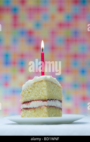 Tranche de gâteau d'anniversaire avec une bougie allumée contre un fond pastel coloré Banque D'Images